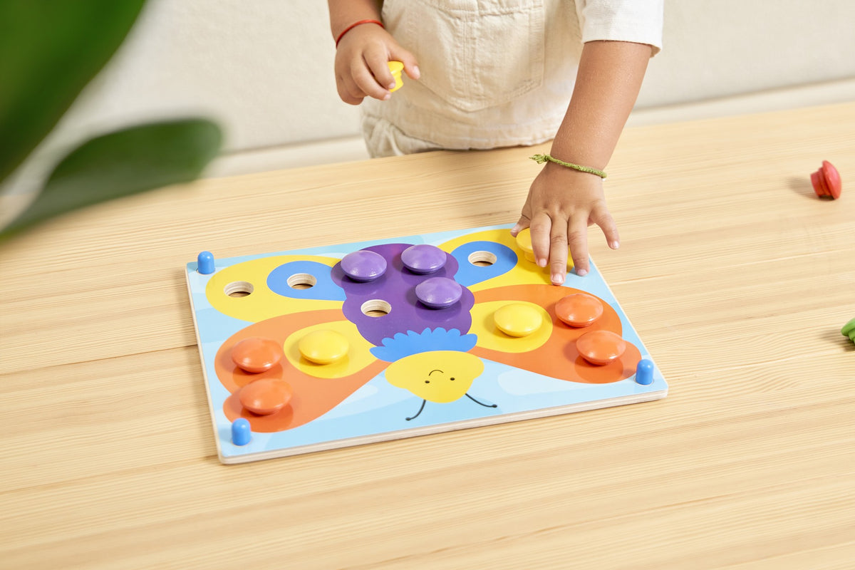 Overhead view of the complete classic Color Button Board butterfly picture, with colourful wooden pegs and a child's hands